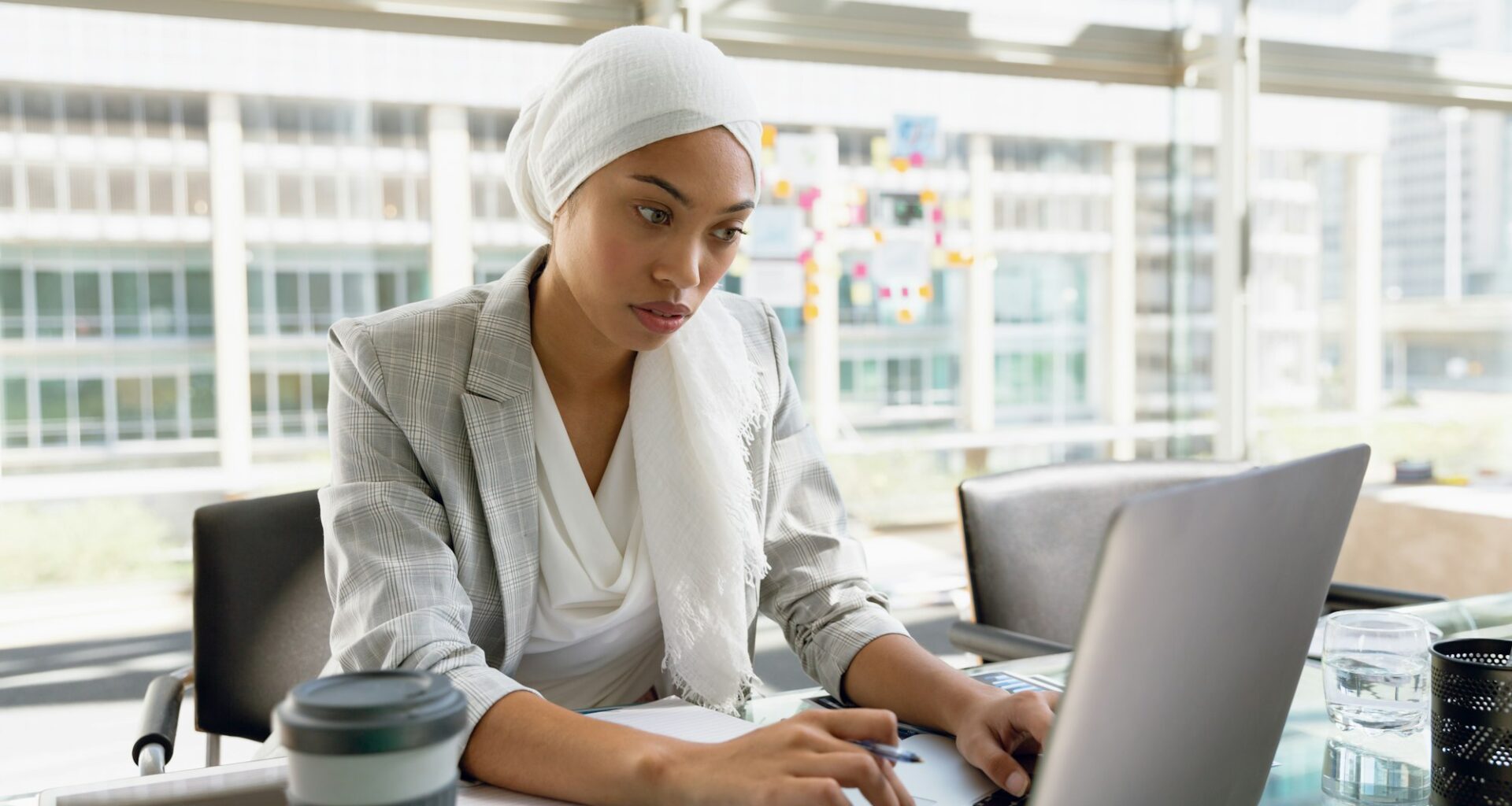 Businesswoman in hijab working on laptop at desk in a modern office